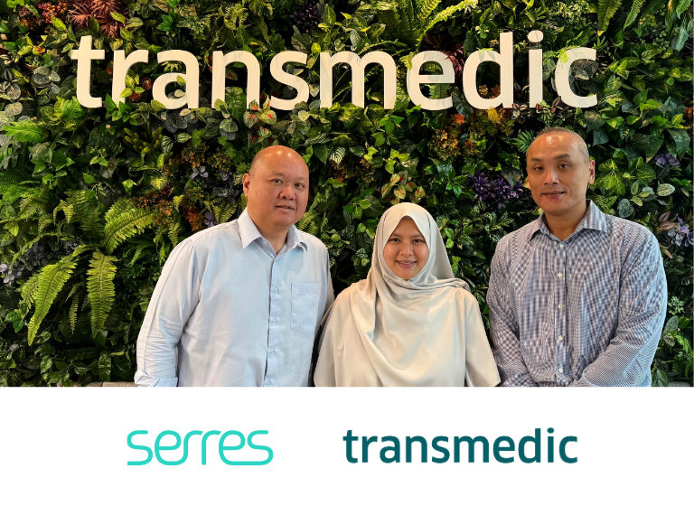 Three people from Transmedic standing in front of the Transmedic logo.