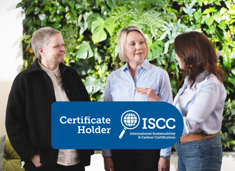 Three people discussing in front of a green plant wall. In front, the ISCC Plus logo.
